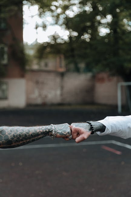Two tattooed arms fist bump outdoors, symbolizing friendship or solidarity.